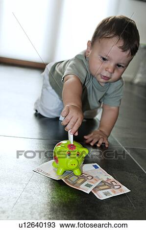 Stock Image - Baby boy putting money in the piggy bank. Fotosearch