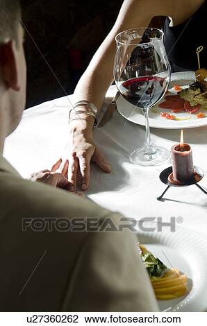 Stock Image - Closeup of couple at dinner table with hands touching. Fotosearch