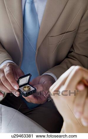 Stock Image - Closeup of hands of young man giving a ring to young woman. Fotosearch