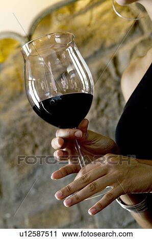 Stock Image - Closeup of red wine in a glass held by young woman's hands. Fotosearch