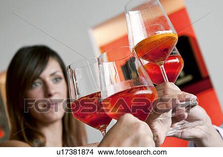 Picture - Closeup of young woman's face and other people's hands holding wine glasses and toasting. Fotosearch