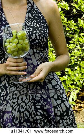 Stock Image - Torso of young woman in vineyard with a wineglass of white grapes. Fotosearch