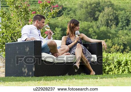 Stock Photo - Young couple sitting on couch in vineyard with white wine. Fotosearch