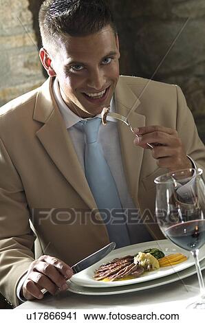 Stock Image - Young man eating with glass of wine at a restaurant. Fotosearch