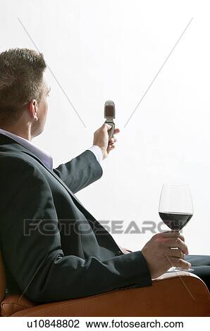 Stock Image - Young man in business suit sitting with glass of red wine and mobile phone. Fotosearch