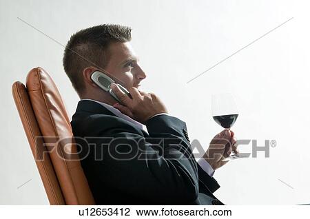 Young man in business suit sitting with glass of red wine and mobile phone View Large Photo Image Stock Image - Young man in business suit sitting with glass of red wine and mobile phone. Fotosearch