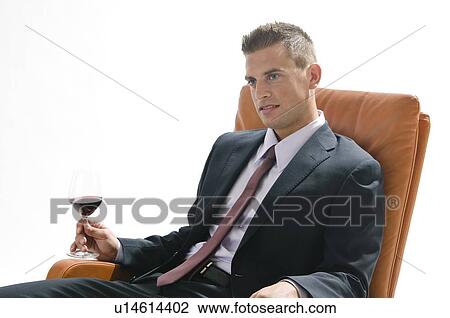 Stock Image - Young man in business suit sitting with glass of red wine. Fotosearch