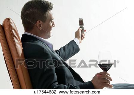 Young man in business suit sitting with glass of red wine and mobile phone View Large Photo Image Stock Image - Young man in business suit sitting with glass of red wine and mobile phone. Fotosearch