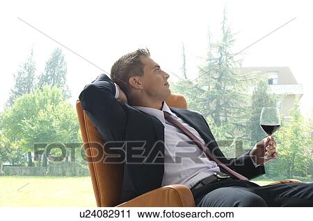 Stock Image - Young man in business suit sitting with glass of red wine. Fotosearch