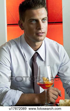 Stock Photo - Young man in business suit sitting with glass of orange wine. Fotosearch