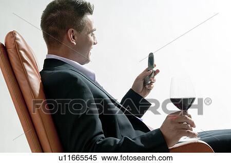 Stock Photography - Young man in business suit sitting with glass of red wine and mobile phone. Fotosearch