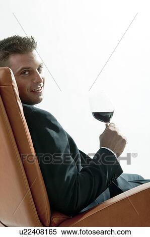 Stock Photography - Young man in business suit sitting with glass of red wine. Fotosearch