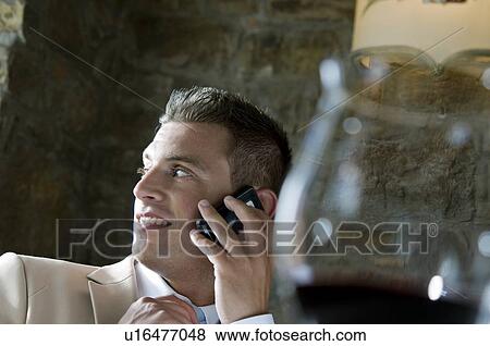 Young man in suit sitting with mobile phone at a restaurant View Large Photo Image Stock Photo - Young man in suit sitting with mobile phone at a restaurant. Fotosearch