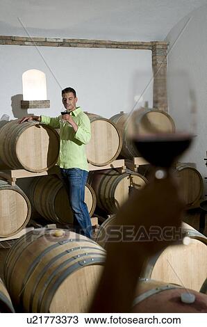 Stock Image - Young man in wine cellar with young woman's hand holding glass of red wine. Fotosearch