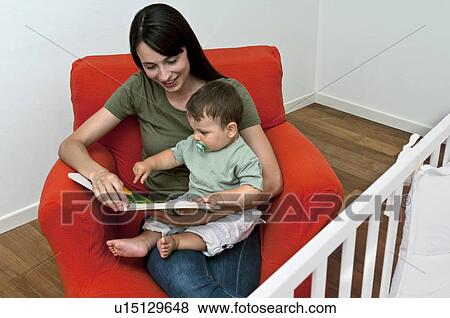 Stock Photo - Young woman and baby boy sitting on arm chair reading a book. Fotosearch
