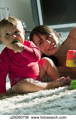 Young woman and baby boy sitting on rug chewing on and playing with toys View Large Photo Image Stock Photograph - Young woman and baby boy sitting on rug chewing on and playing with toys. Fotosearch