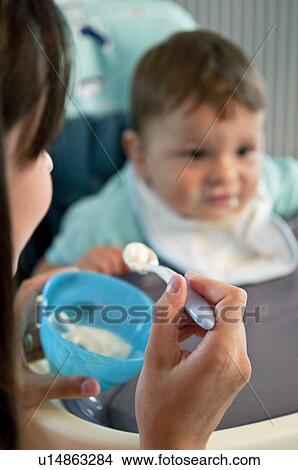 Young woman feeding baby boy in high chair View Large Photo Image Picture - Young woman feeding baby boy in high chair. Fotosearch