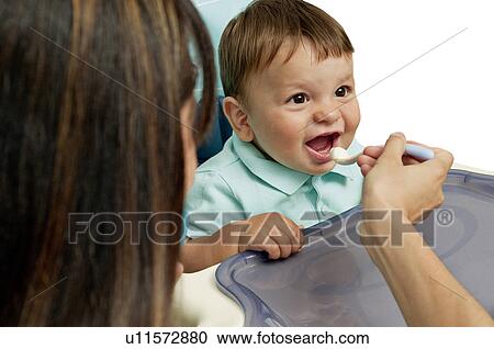 Young woman feeding baby boy in high chair View Large Photo Image Stock Image - Young woman feeding baby boy in high chair. Fotosearch