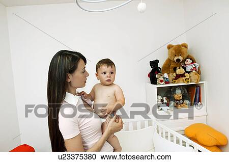 Stock Image - Young woman holding baby boy in bedroom. Fotosearch
