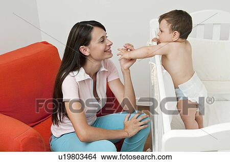 Young woman on arm chair holding hands with baby boy in crib View Large Photo Image Picture - Young woman on arm chair holding hands with baby boy in crib. Fotosearch