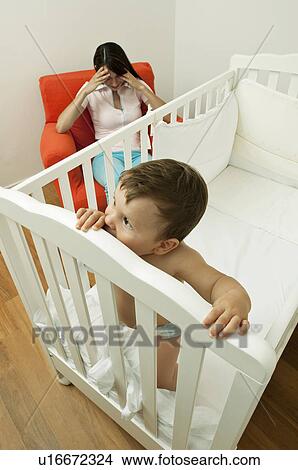 Young woman on arm chair holding her head and baby boy in crib View Large Photo Image Picture - Young woman on arm chair holding her head and baby boy in crib. Fotosearch