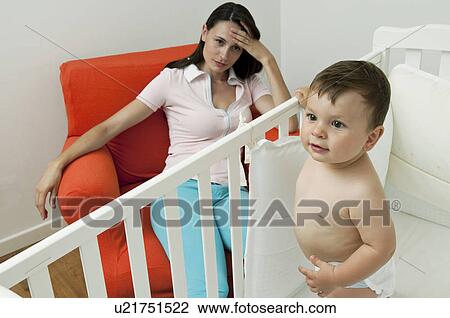 Young woman on arm chair holding her head and baby boy in crib View Large Photo Image Stock Image - Young woman on arm chair holding her head and baby boy in crib. Fotosearch