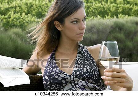 Stock Photograph - Young woman sitting in vineyard with white wine and a book. Fotosearch