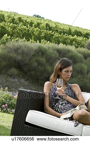 Young woman sitting on couch in vineyard with white wine reading a book View Large Photo Image Stock Photograph - Young woman sitting on couch in vineyard with white wine reading a book. Fotosearch