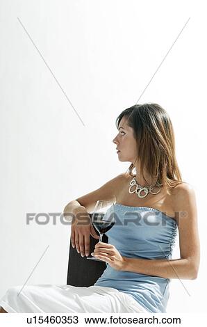 Stock Image - Young woman sitting with glass of red wine. Fotosearch