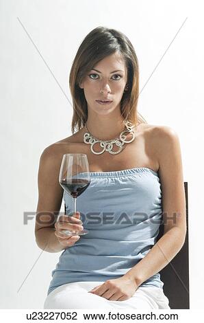 Stock Image - Young woman sitting with glass of red wine. Fotosearch