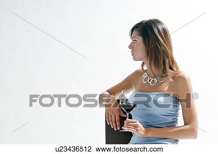 Stock Image - Young woman sitting with glass of red wine. Fotosearch