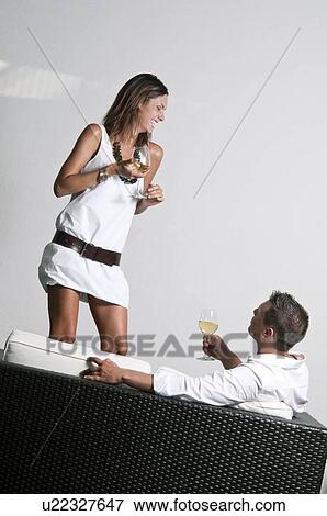 Young woman with white wine standing next to couch with young man and wine View Large Photo Image Stock Photo - Young woman with white wine standing next to couch with young man and wine. Fotosearch