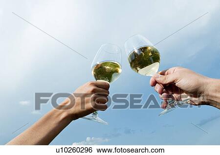 Stock Photograph - Young woman's and young man's hands holding wineglasses with white wine and toasting. Fotosearch