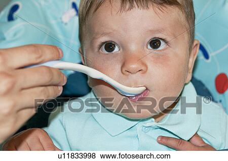 Stock Photo - Young woman's hand feeding baby boy in high chair. Fotosearch