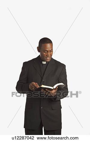 Stock Image - a man wearing a clerical collar and reading from his bible. Fotosearch