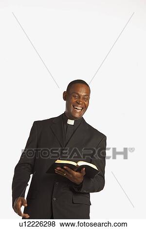 Stock Photo - a man wearing a clerical collar and laughing while holding an open bible. Fotosearch