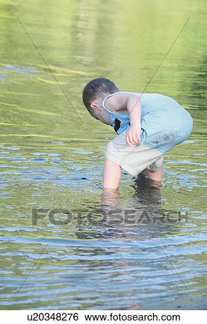 Stock Photograph - a young boy playing in the shallow water. Fotosearch
