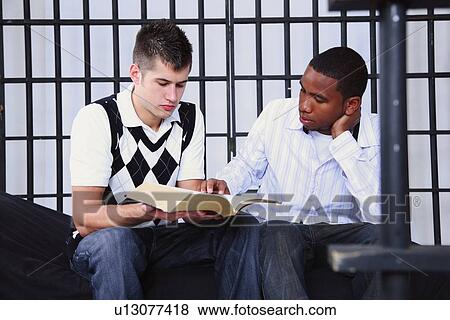 Stock Photo - a young man reading the bible to another young man in jail. Fotosearch