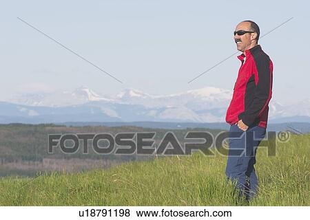 Stock Photo - calgary, alberta, canada; a male hiker overlooking the valley with mountains. Fotosearch