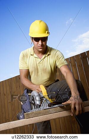 Stock Image - Construction Worker Sawing Wood. Fotosearch
