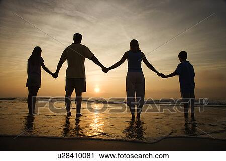 Stock Image - Family Holding Hands on Beach Watching the Sunset. Fotosearch