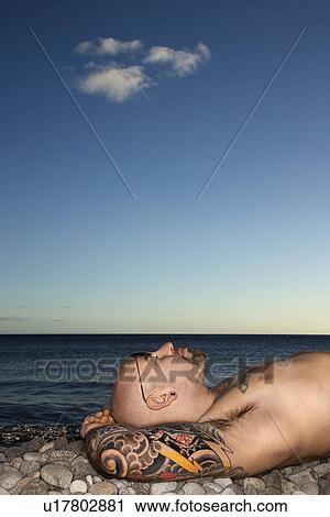 Stock Image - Tattooed Man Lying on Beach. Fotosearch
