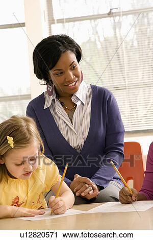 Stock Image - Teacher Smiling and Helping Students With Schoolwork . Fotosearch