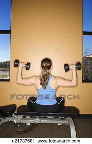Stock Image - Woman Seated Lifting Weights. Fotosearch