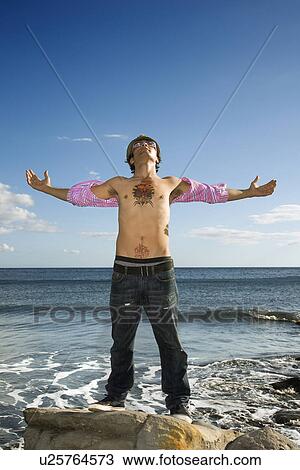 Stock Image - Young Man Standing on Ocean Rock with Arms Outstretched. Fotosearch
