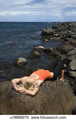 Stock Photography - Young Woman Lying on Rock at Beach. Fotosearch