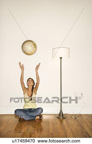 Stock Image - Young Woman Smiling and Sitting Tossing a Globe. Fotosearch
