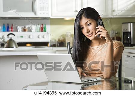 Stock Photography - Young Woman Using Laptop and Talking on Cellphone. Fotosearch