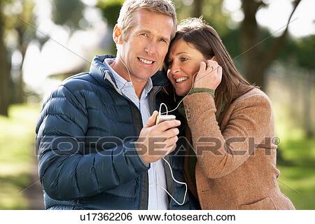 Stock Photograph - Couple Listening To MP3 Whilst Walking In Autumn Park. Fotosearch