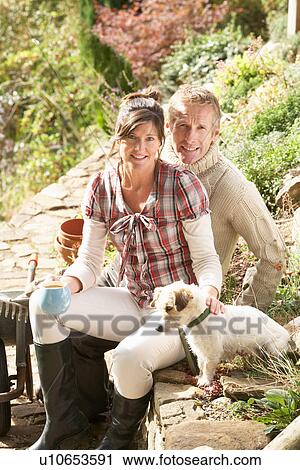 Stock Image - Couple With Dog Having Coffee Break Whilst Working Outdoors In Garden. Fotosearch